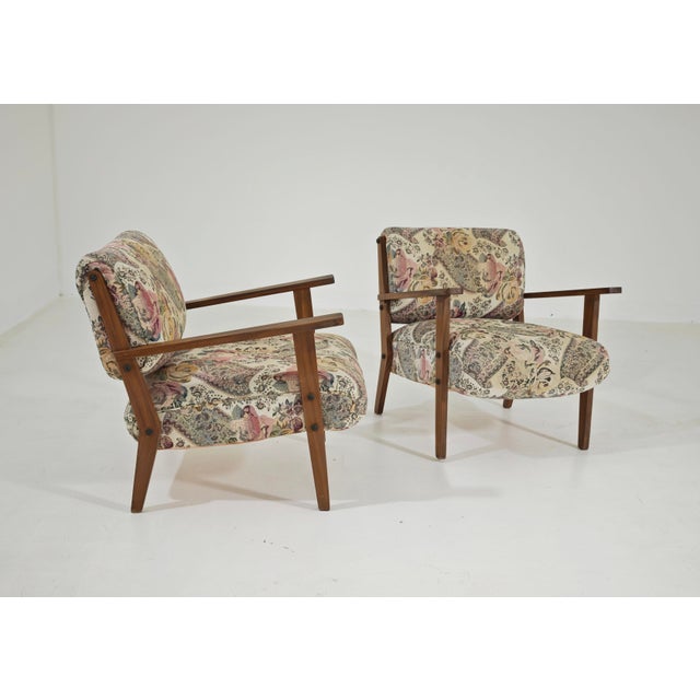A stunning pair of vintage armchairs, mostly from the 1960s, featuring a solid wooden frame and fabric upholstery with...