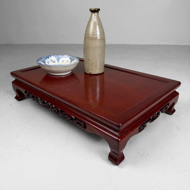 An elegant Japanese display stand in warm reddish-brown lacquered wood, with refined openwork carving and gracefully...