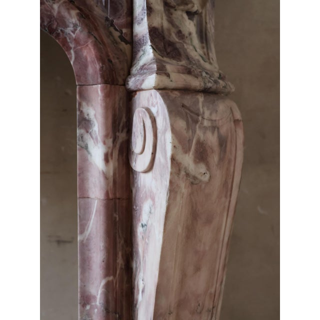 Antique fireplace crafted from Violet de Villette marble, featuring a color palette of soft pink and purple tones with...