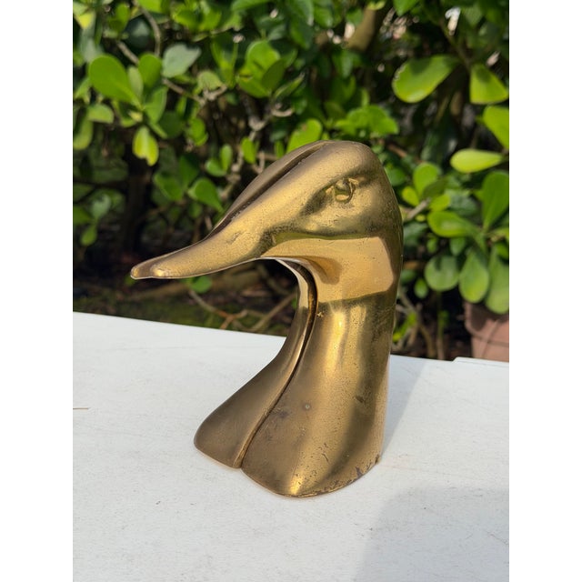 Vintage pair of sculptural duck bookends in an aged brass finish. Each bookend features a highly stylized, elongated duck...