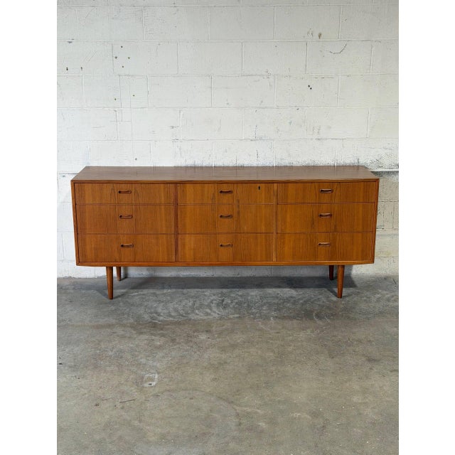This minimalist lowboy features a wide rectangular frame with a symmetrical configuration of nine stacked storage drawers...