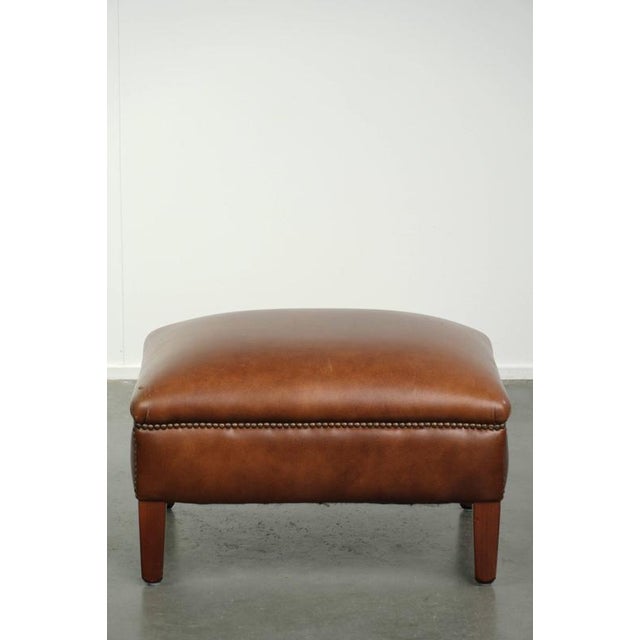 This ottoman is made of cowhide leather in a warm cognac color and is finished with decorative nails. A footstool, also...