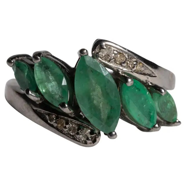 A ring of clustered marquise emeralds graduating down from a larger center gemstone. Bordered at the top and bottom with...