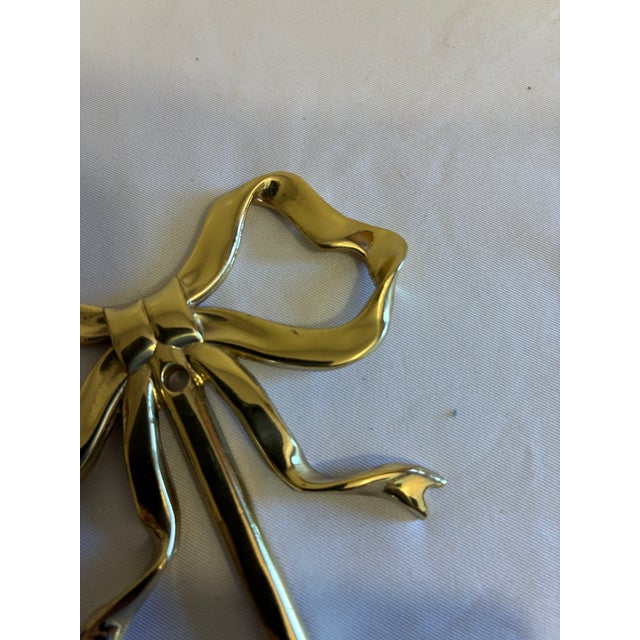 A charming vintage brass wall hook formed as a sculptural ribbon bow. Graceful loops, knotted center, and trailing ribbon...