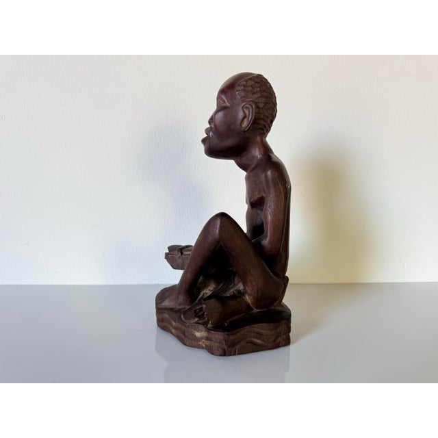 This exquisite vintage African art piece showcases a hand-carved wooden figure, elegantly depicting a seated musician. The...