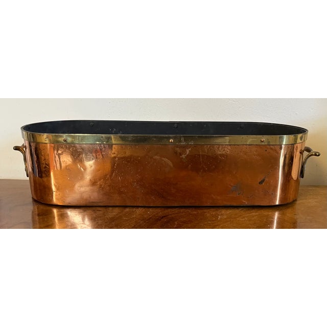 Antique English copper long oval jardiniere planter with brass trim at the rim and handles at the ends. Measures 18 1/4"...