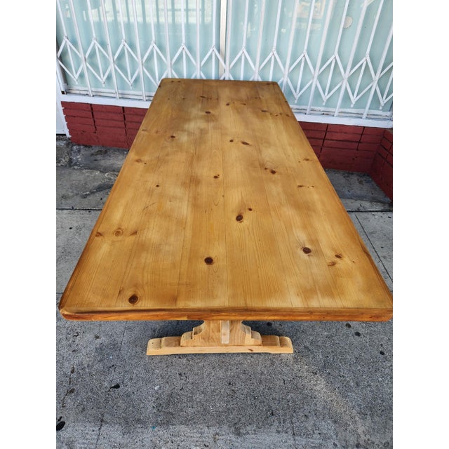 Solid pine dining table has a light honey finish and a classic trestle base. The rectangular tabletop features visible...