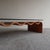 Low table with a steam-bent laminated wood base in a warm terracotta finish, shaped into a continuous undulating wave....
