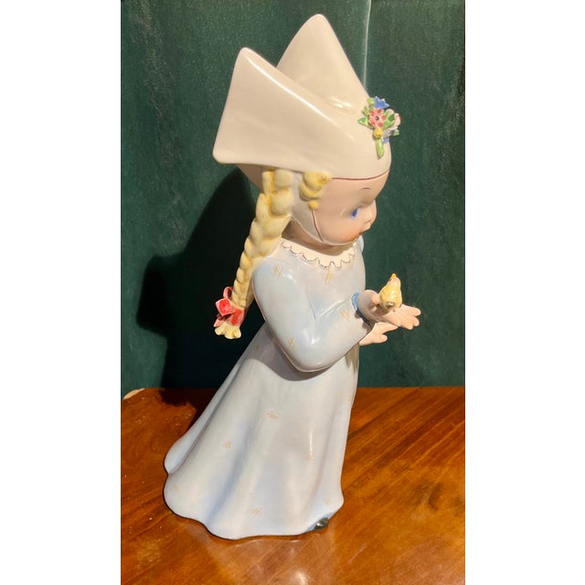 Tosin ceramic depicting a girl with braids and a veil on her head and holding a little bird, title of the work...