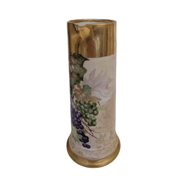 This antique Limoges tankard pitcher features a tall, slender cylindrical body with a flared pedestal base, an elegant...