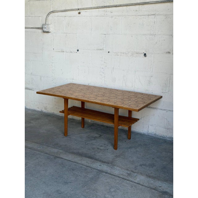 This Danish oak coffee table pairs a long rectangular form with a patterned ceramic tile top. A lower slatted shelf spans...