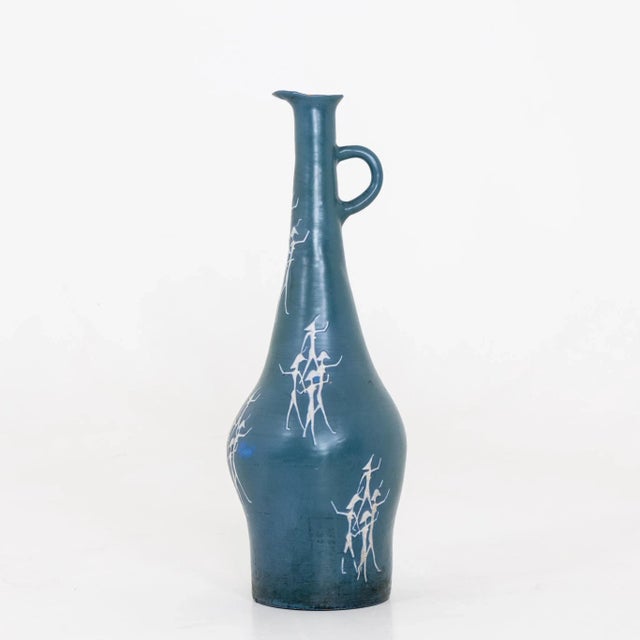Large ceramic vase with blue overlay and white figures on the wall. Signed illegibly on the bottom.