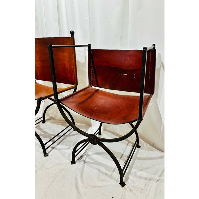 Two striking Savonarola-inspired chairs (one arm, one side) featuring rich saddle leather slung over sculptural iron...