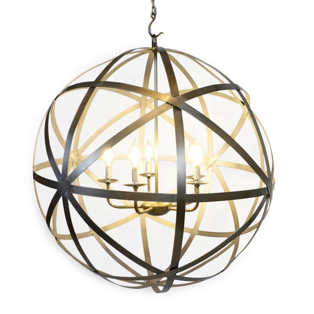 Crafted from iron with a warm brass finish, this striking globe-shaped chandelier features intersecting metal bands...