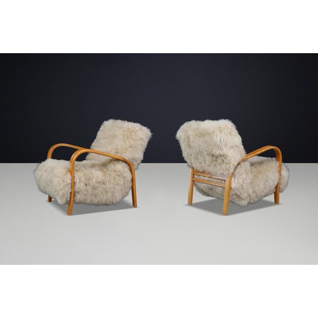 A sculptural pair of Czech bentwood lounge chairs by Kozelka & Kropáček, upholstered in soft ecru Tibetan sheepskin....