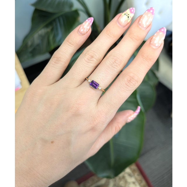 A vibrant emerald-cut amethyst (7×5mm) sits elegantly at the center, framed by sparkling natural diamond accents and...