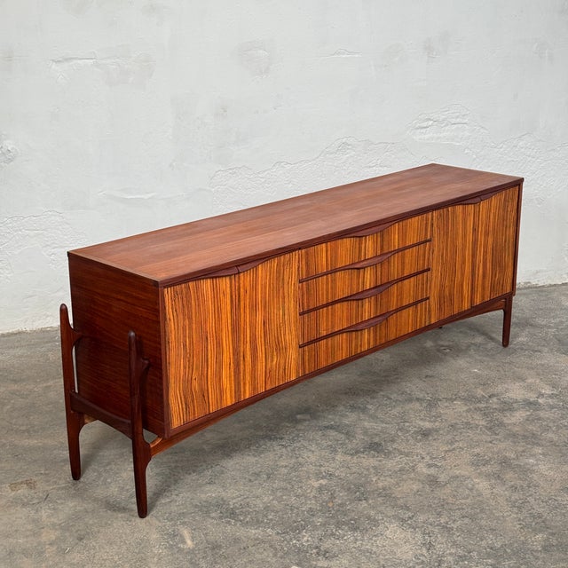 This exceptional 1960s sideboard is a masterclass in british mid-century craftsmanship, produced by the prestigious...
