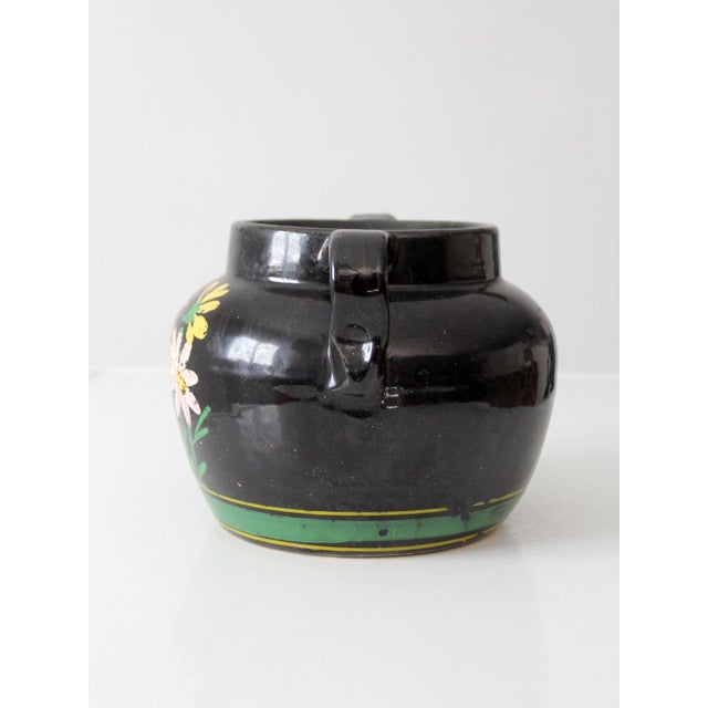 A vintage hand-painted pottery vessel with a glossy black glaze, colorful garden flowers and bold green banding. The...