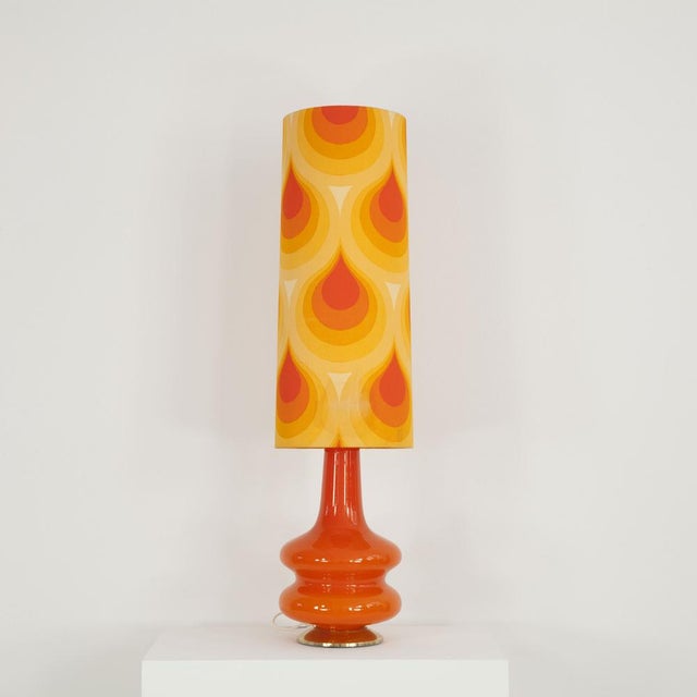 This floor lamp was made in the 1970s. It consists of an illuminated glass foot and a fabric screen with typical 70ies...