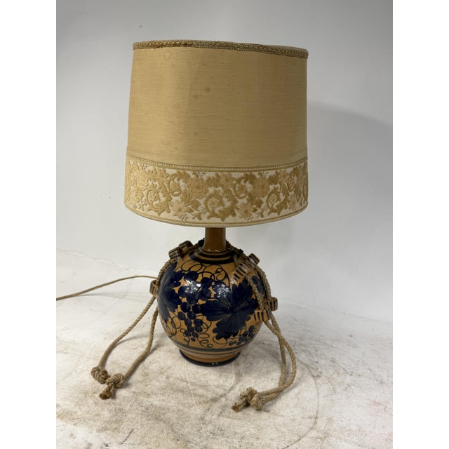 Beautiful 1950s table lamp with a terracotta base, hand-painted floral motifs, and woven rope handles. The lampshade is...