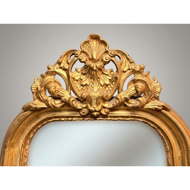 A super long and slender French-inspired gilt wood mirror featuring an elegant arched top topped with an ornate carved...