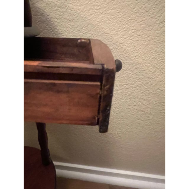 Vintage three-tier round accent table featuring turned spindle legs, a pull-out storage drawer, and raised gallery rails...