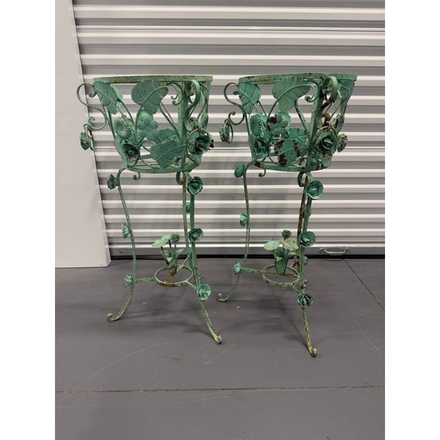 A dramatic pair of verdigris wrought iron plant stands, featuring a floral and leaf motif with dangling rosettes. Standing...