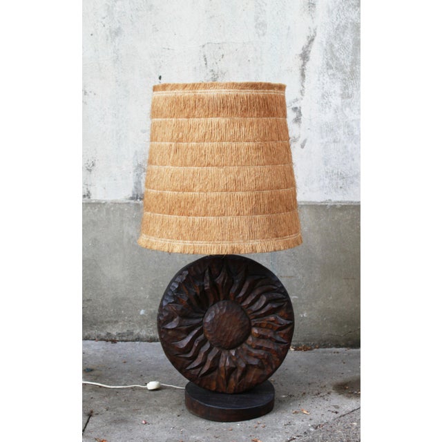 A brutalist table lamp by delsinne, featuring a solid wood base sculpted in relief to evoke a stylized sun. The base, with...