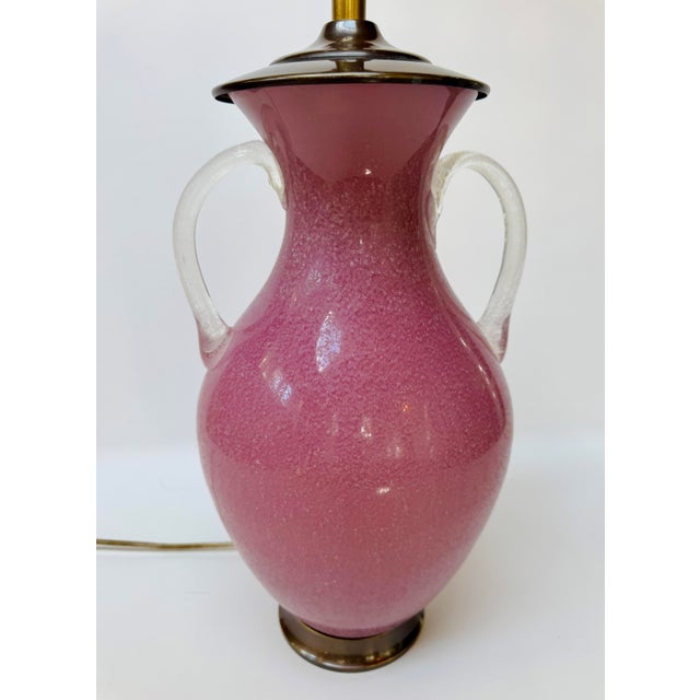Vintage Chapman table lamp with a rich pink glass body, clear loop handles, and dark brass-tone mounts. The rounded urn...
