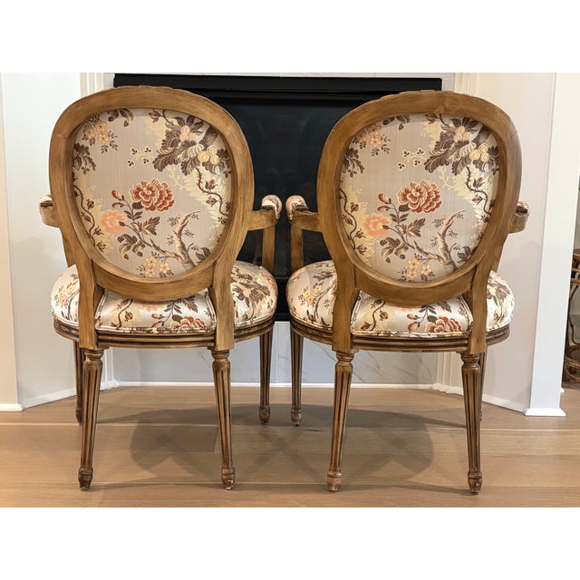 An elegant pair of vintage Louis XVI style carved wood fauteuil armchairs in floral chinoiserie upholstery. The chairs are...