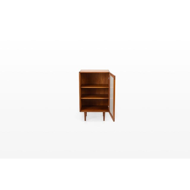 Elegant Danish vintage display cabinet crafted from teak wood. Featuring a glass door and two wooden shelves, this piece...