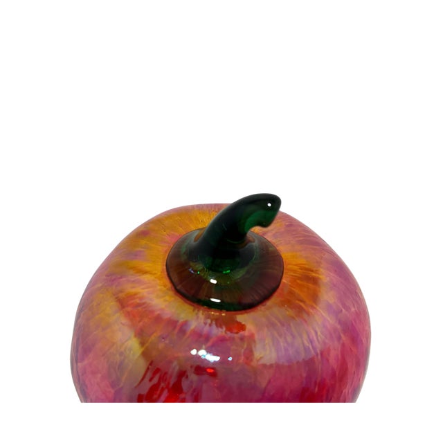 A beautiful red and gold iridescent art glass apple paperweight featuring rich shades of red, pink, and gold with a...
