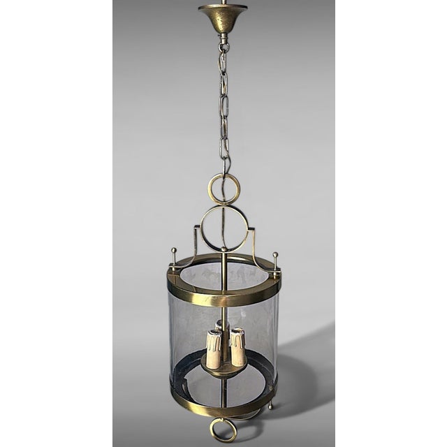 Elegant French suspended lantern crafted in brass with a transparent blown glass cylindrical diffuser. This piece...