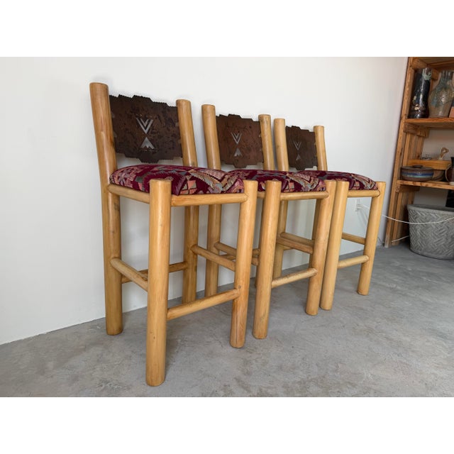 A striking set of three vintage Southwestern bar stools featuring solid rustic log construction and distinctive...