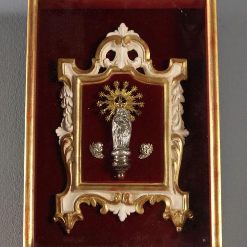 Statue of the Madonna and Child in silver-plated metal mounted on a gilded and white lacquered wooden frame. Garnet red...