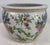 Floral cache pot features blue, yellow and pink flowers with green leaf accents. Asian style planter has a floral motif on...