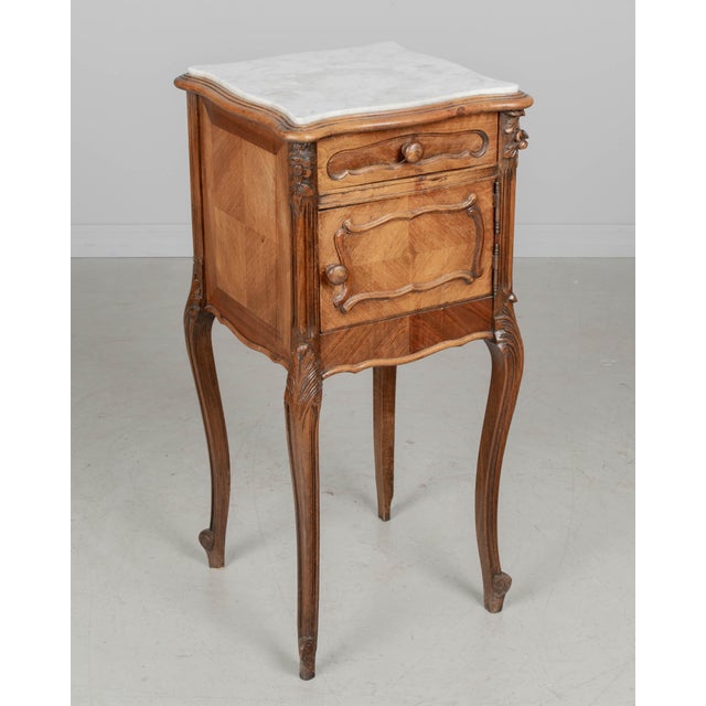 A French Loius XV style marble top nightstand or bedside cabinet. Crafted from solid walnut with hand-carved floral corner...