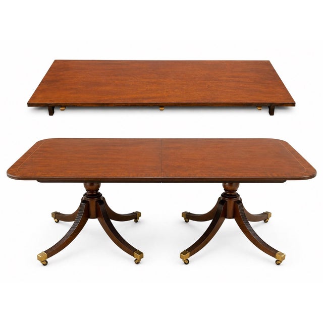 An elegant Baker Furniture heirloom dining table in the Georgian/Regency manner, featuring a banded mahogany top, carved...