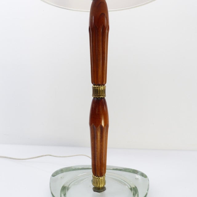 The lamp rests on an imposing triangular base with rounded corners, made of solid, clear glass with a subtle aqua tint,...