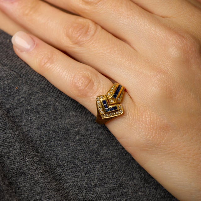 This vintage sapphire and diamond ring is a refined interplay of color, structure, and classic design. A row of square cut...