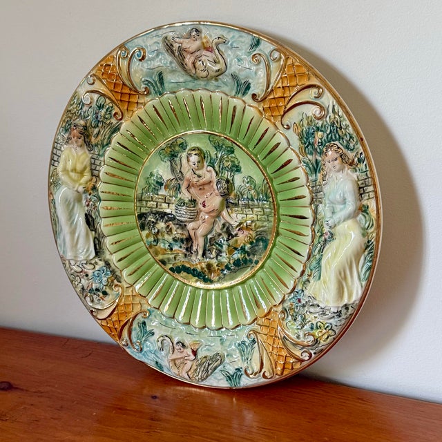Midcentury Italian Capodimonte plate with hand-painted relief of cherubs, ladies, and swans in a garden, accented with...