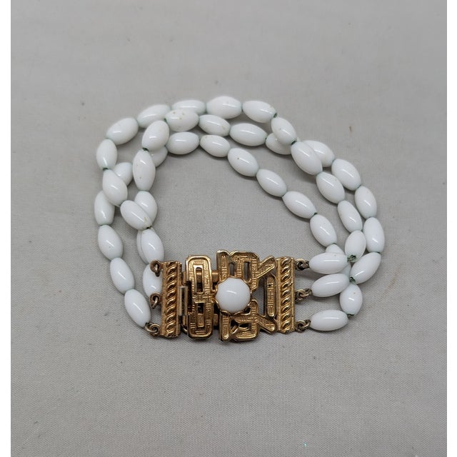 Hard to find 1960s goldtone 3-strand white ovoid bead with asian character with white rhinestone cabochon in the middle of...