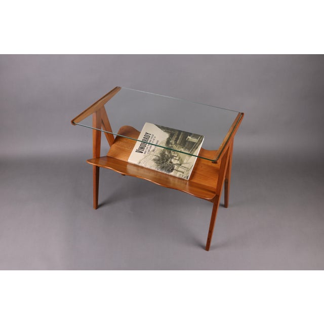 This elegant Italian side table from the 1960s features a beautifully sculpted wooden frame with dynamic, angular legs and...