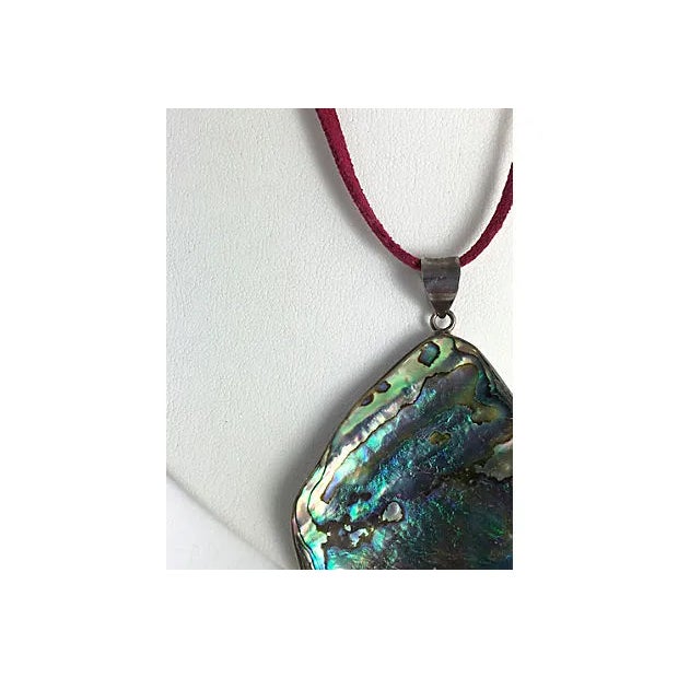 Free form piece of abalone shell set into a silver frame with a silver bale hanging from a cord necklace that must be tied...
