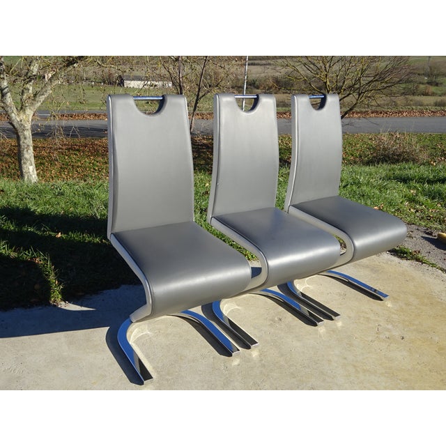 Set of 3 designer chairs, upholstered in grey faux leather with white trim highlighting the Z-shaped profile. High...