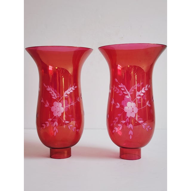 Pair of cranberry glass hurricane lamp shades featuring an etched foral design with flare top and 1" 5/8 fitter bases.