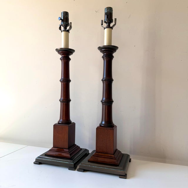 Vintage pair of colonial style turned mahogany lamps with bronze bases. The pair are in a dark warm walnut and solid. The...