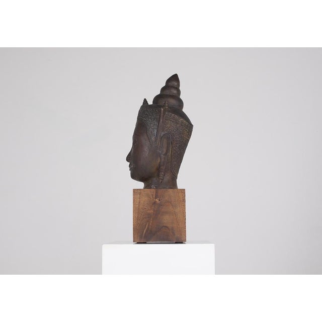 Copper alloy sculpture of a Buddha head, Thailand, 20th century. The Buddha head is presented on a solid wood base. Claude...
