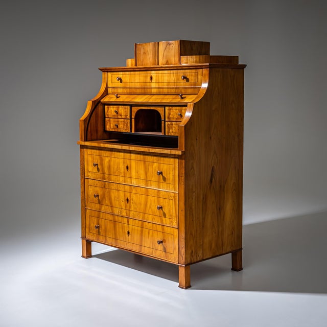 Biedermeier roll-top secretary raised on block-mounted square legs and fitted with three drawers in the lower section....