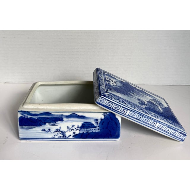 Here is a vintage blue and white porcelain lidded trinket box featuring an idyllic landscape with pavilions, mountains,...